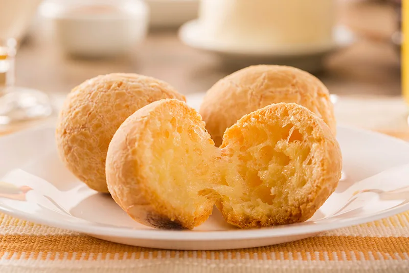 Pao de queijo partido ao meio. Ele é redondinho e tem cor amarela.