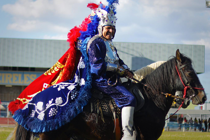 Homem com túnica da cor azul, montado no cavalo.
