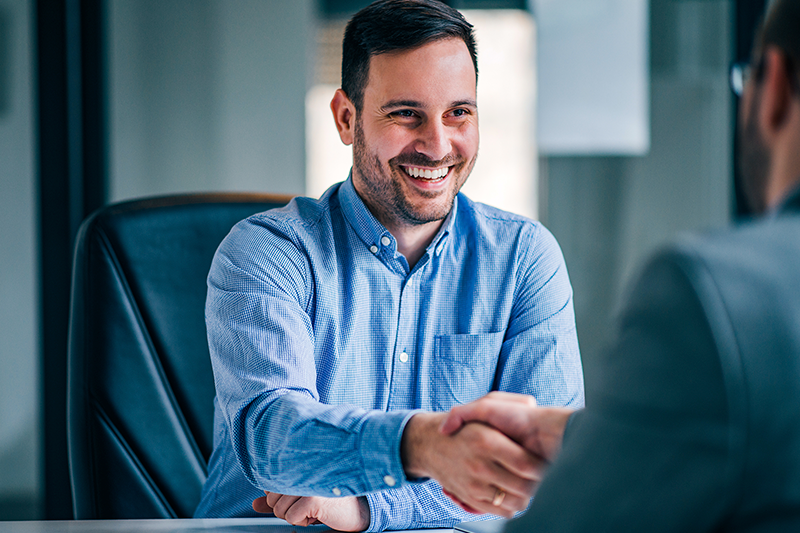 Homem sorrindo e apertando a mão de outra pessoa.
