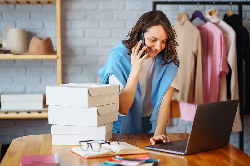 Mulher falando no celular com o computados a sua frente.