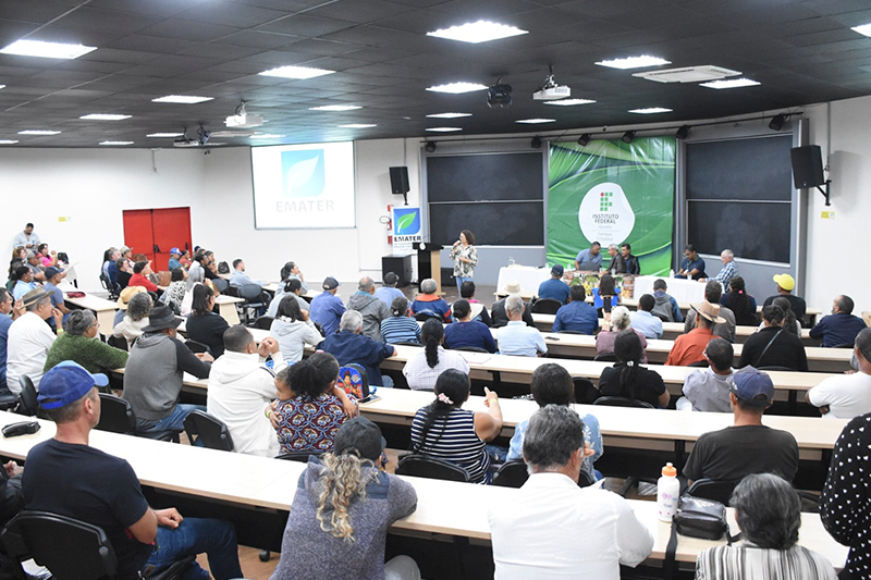 Pessoas sentadas em cadeiras no auditório com atenção no palco.