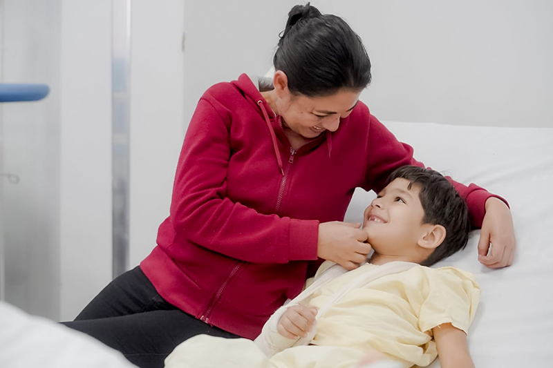 Com a mãe, Lúcia, o pequeno Heitor sorri, em leito do Hecad, após cirurgia bem-sucedida no braço direito. Foto: Iron Braz/SES.